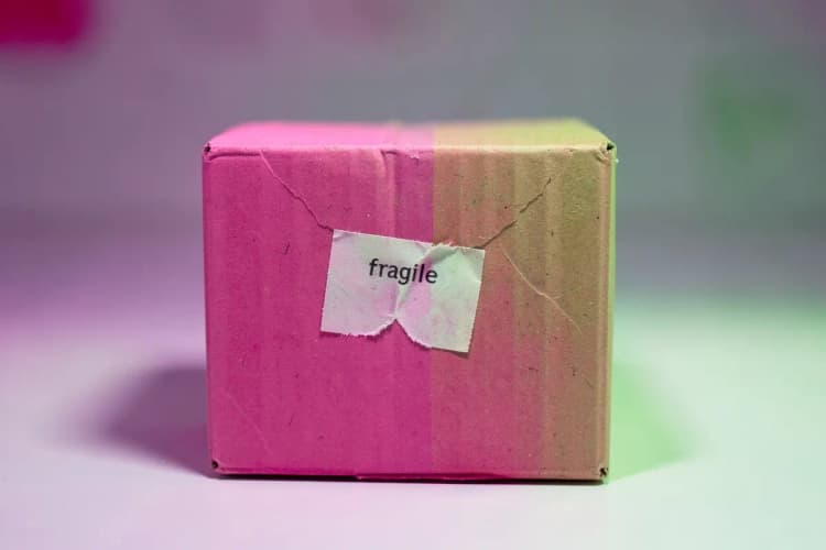 Caixa de papelão amassada com um adesivo de 'frágil' rasgado.
