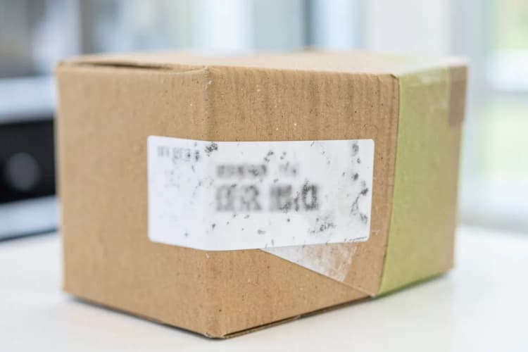 Uma pessoa olhando para uma etiqueta de envio ilegível em uma caixa.