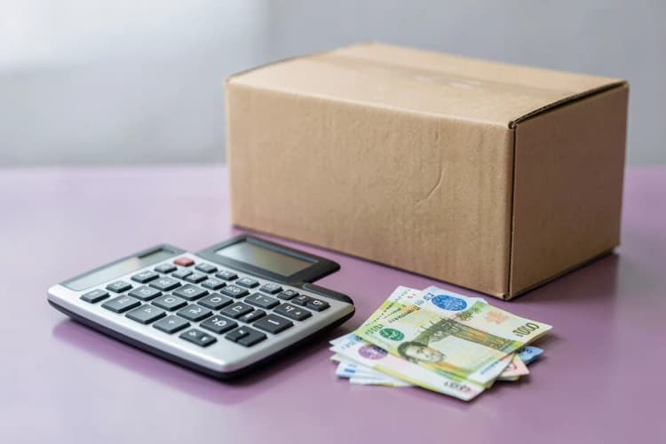 Calculadora e notas de dinheiro sobre uma mesa com uma caixa de papelão ao lado, close-up, luz de escritório, sem pessoas.