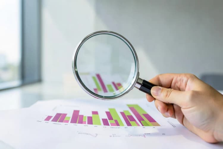 Uma mão segurando uma lupa sobre um gráfico de barras, simbolizando análise de dados.