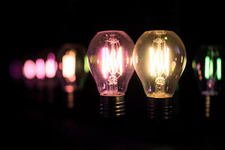 Uma série de lâmpadas incandescentes acesas, com uma delas brilhando mais intensamente, representando ideias e qualidade.