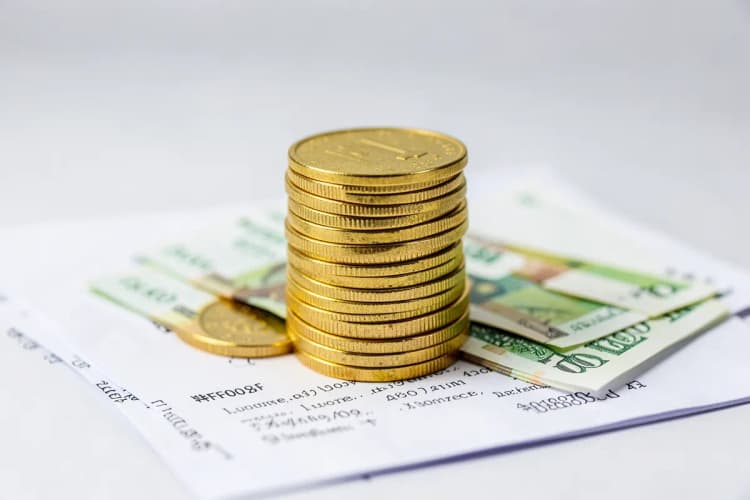 Uma pilha de moedas de ouro e notas de dinheiro empilhadas em cima de um contrato de papel aberto.