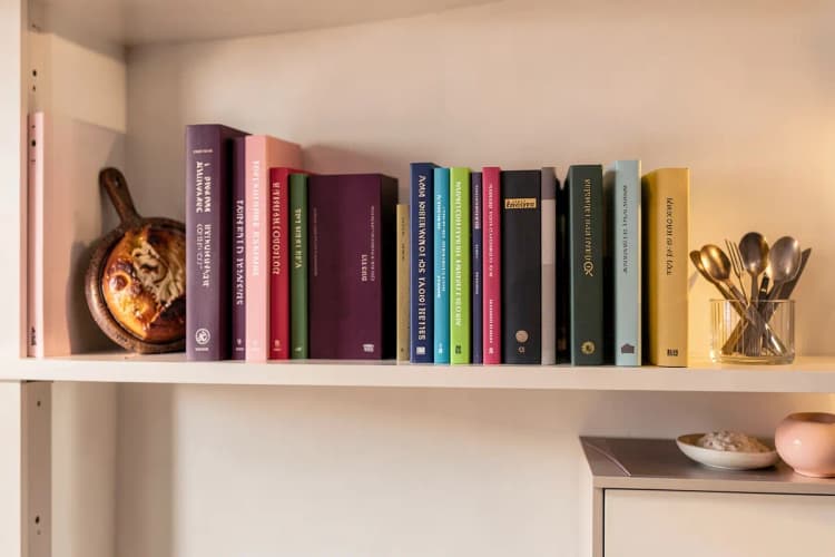Uma prateleira com livros e objetos decorativos representando diferentes áreas de atuação, como culinária, moda e tecnologia.