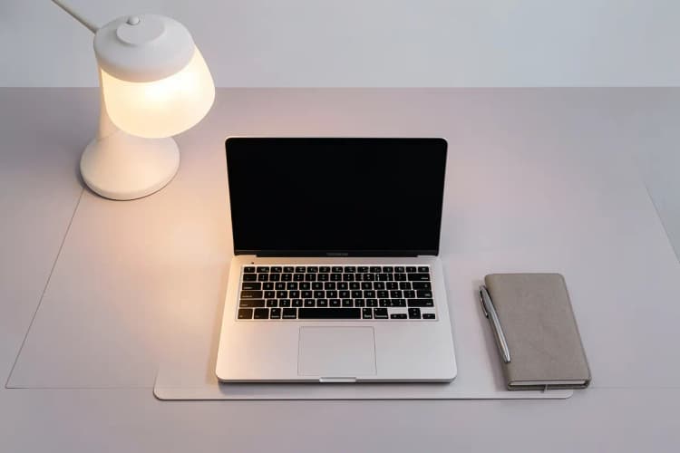 Uma pessoa sentada em uma mesa com um laptop e um caderno aberto.