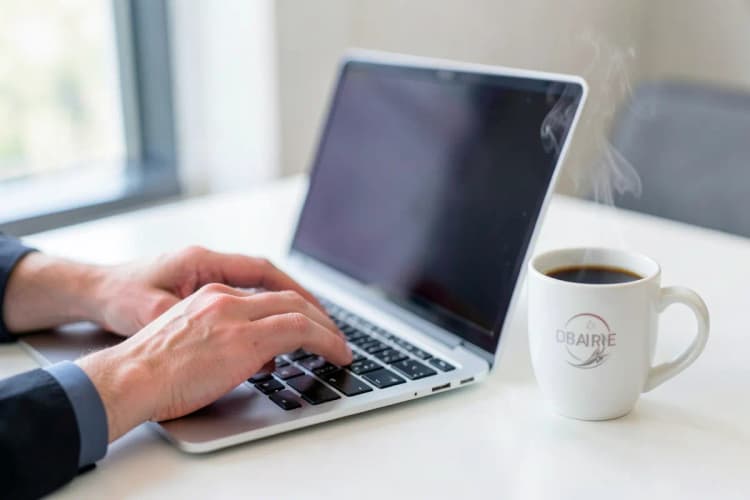 Uma pessoa digitando em um laptop com uma xícara de café ao lado.